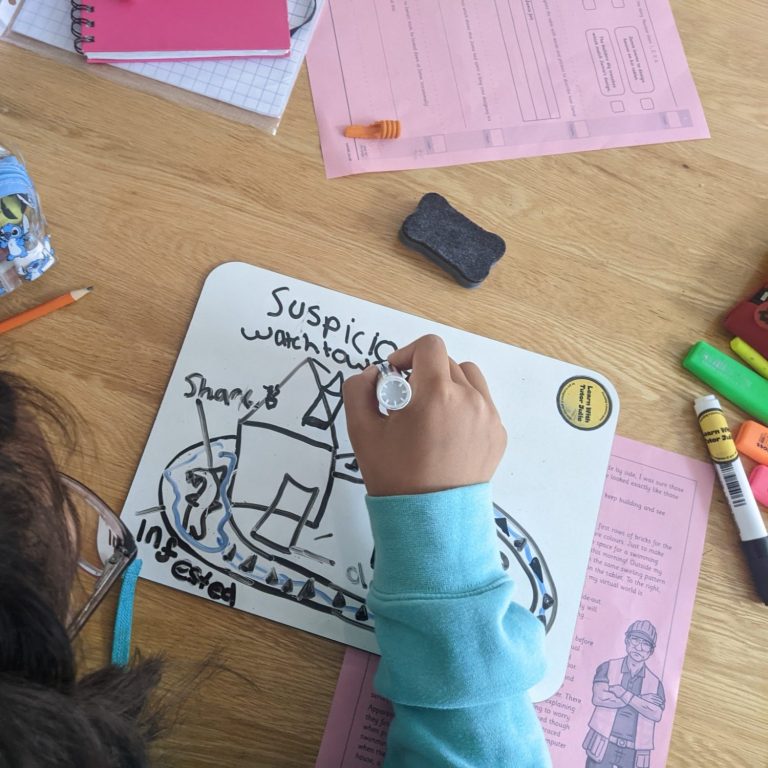 Supporting a child to visualise a written description. Child drawing on a whiteboard with various coloured markers, surrounded by papers and stationery.