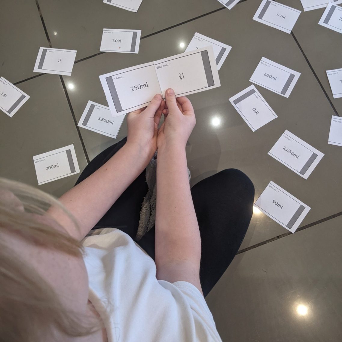 Supporting the learning of measurement equivalents through a game. A child sits on the floor surrounded by scattered cards, holding one card in their hands.
