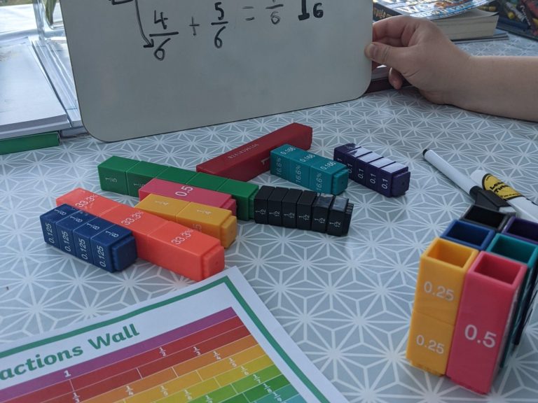 Converting fractions to a common denominator using a fraction wall, fractions blocks and written representation. A table with colourful blocks used for teaching fractions and a written equation.